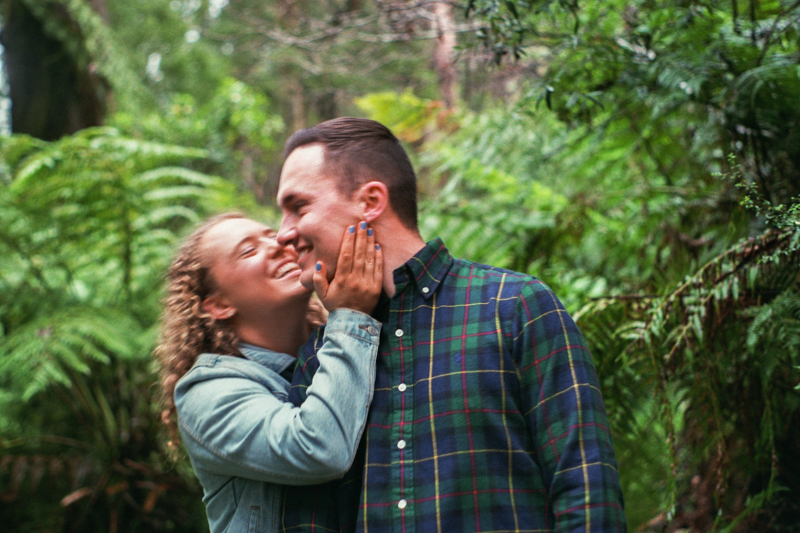 couple kissing on cheek in forest