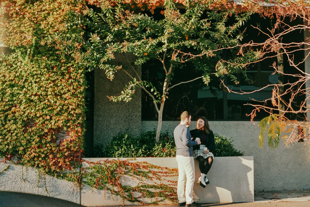 couple sitting surrounded by autumn coloured vines crawling on the walls on the city building behind them