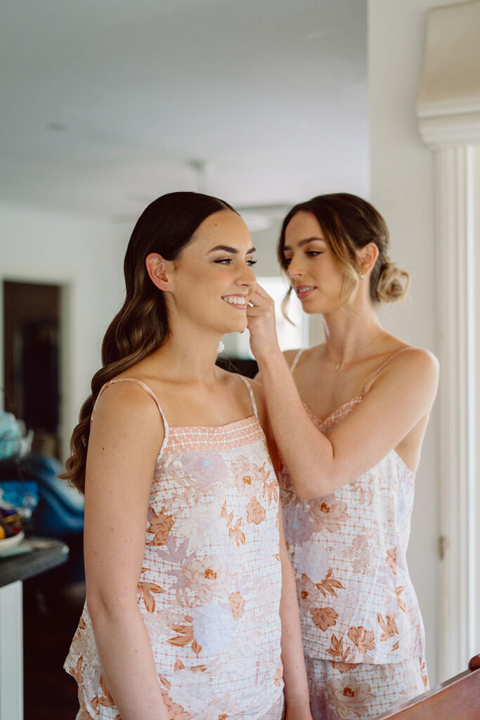 Bride smiling while her bridesmaid helps her put on her earrings