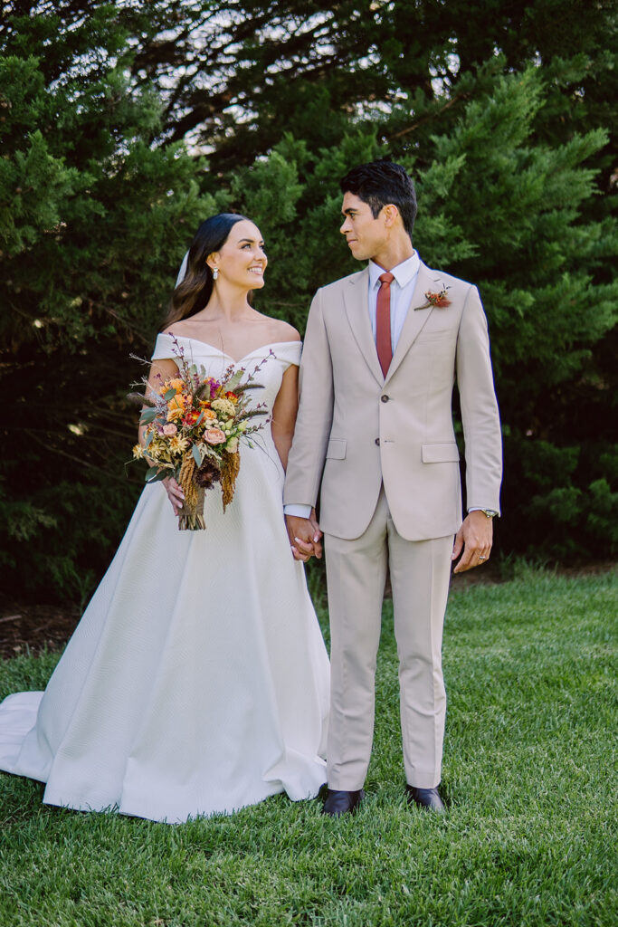 Bride and groom staring into each other's eyes during their wedding portraits in front of a large bush and lush green lawn