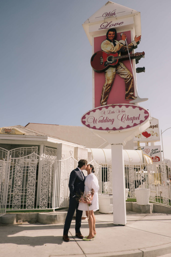 A bride and groom kissing underneath a wedding chapel sign