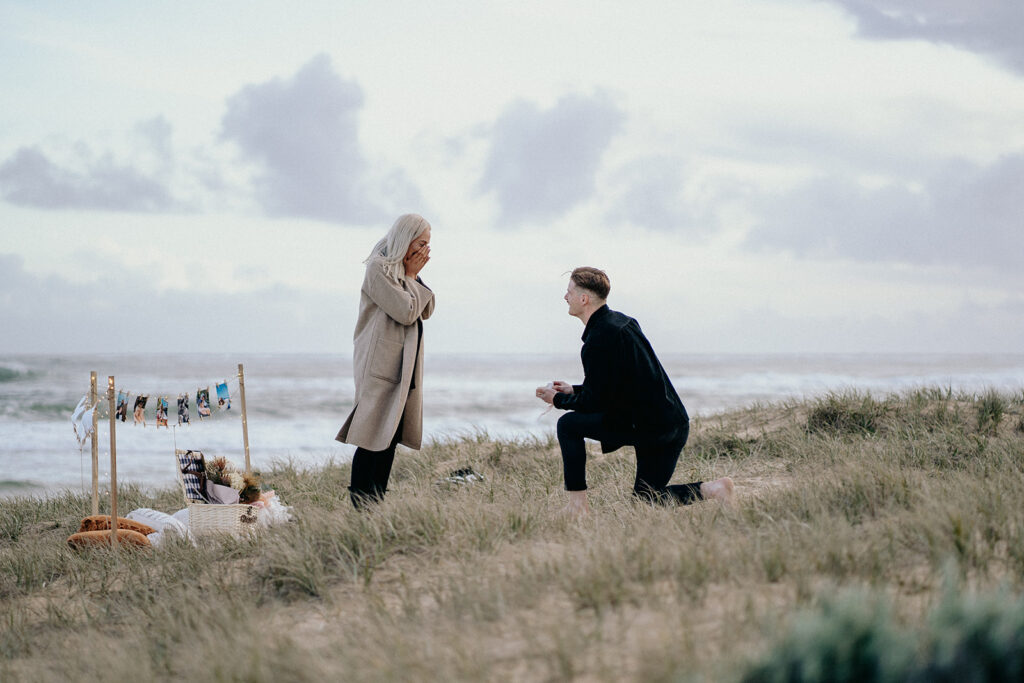 proposal picnic at the beach ideas and inspiration, girl crying, guy on one knee proposing during sunset, sentimental with photos, candles, flowers a letter and fairy lights -3