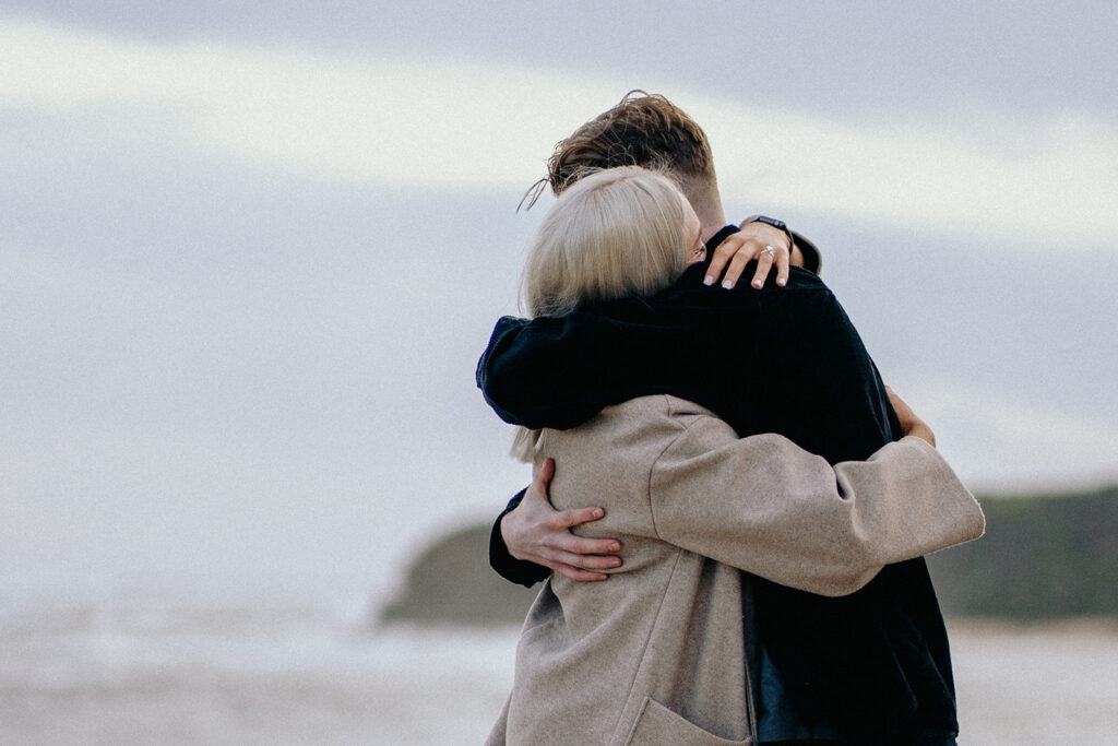 couple hugging and crying after getting engaged, proposal picnic at the beach ideas and inspiration, girl crying, guy on one knee proposing during sunset, sentimental with photos, candles, flowers a letter and fairy lights -3