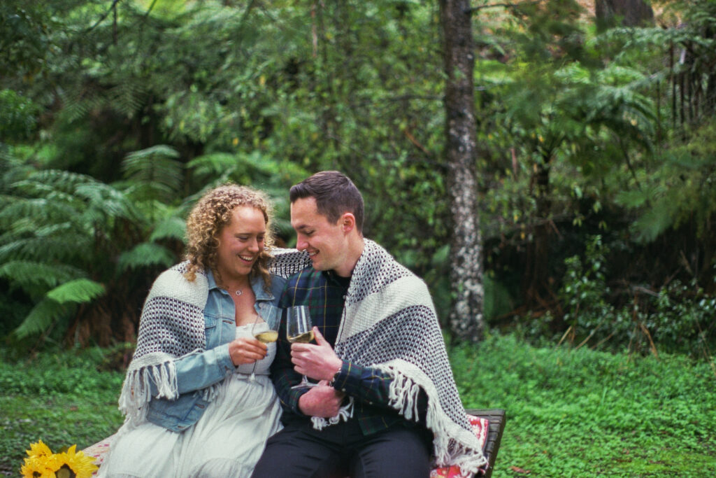 A couple clinking their wine glasses together after pouring a bottle of wine at their engagement session