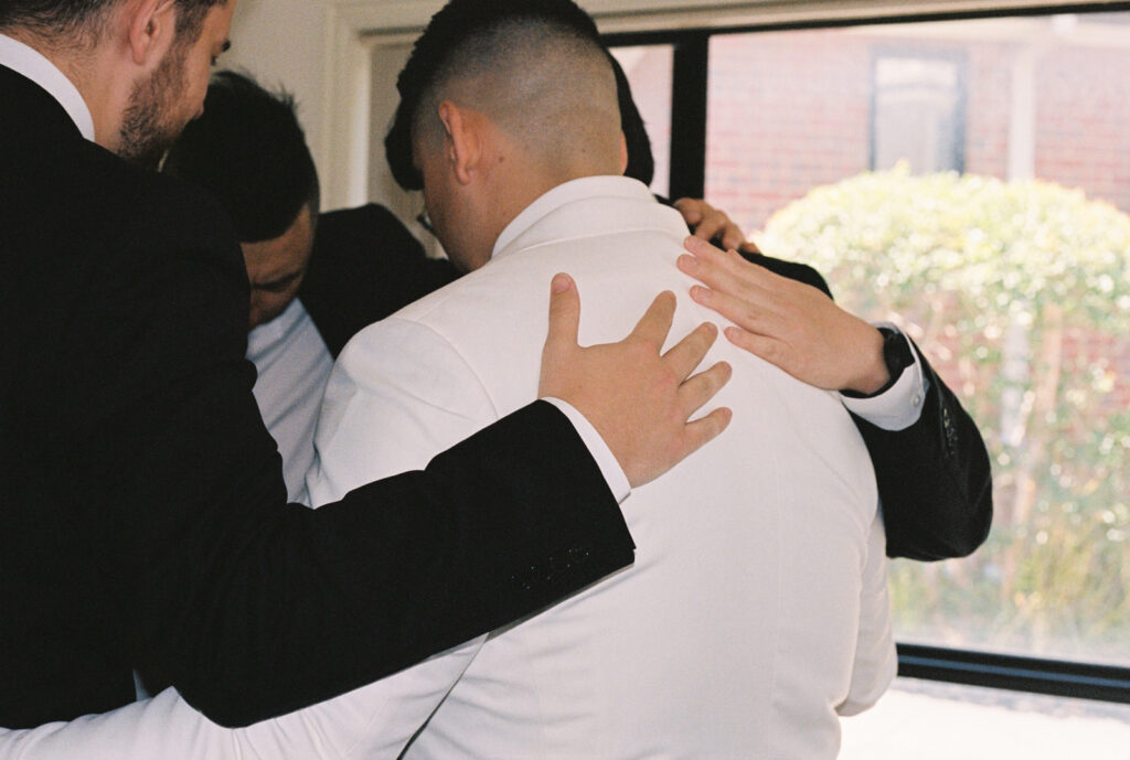 Groomsman praying over groom before his wedding day at emu bottom estate, captured on 35mm film