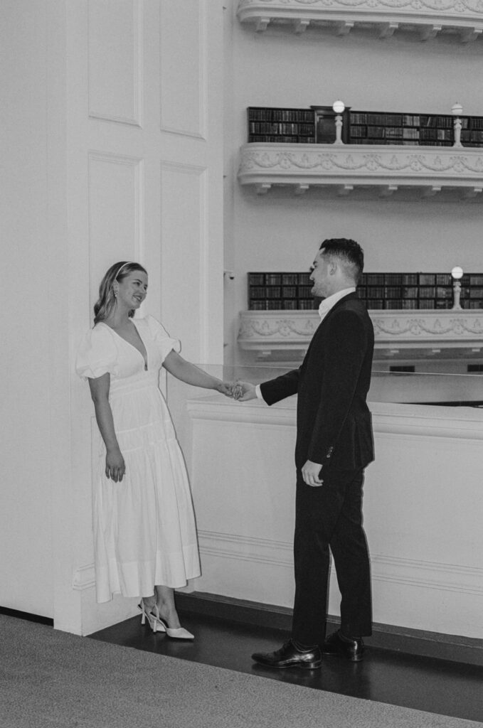 couple holding hands, the books and shelve of the state library behind them