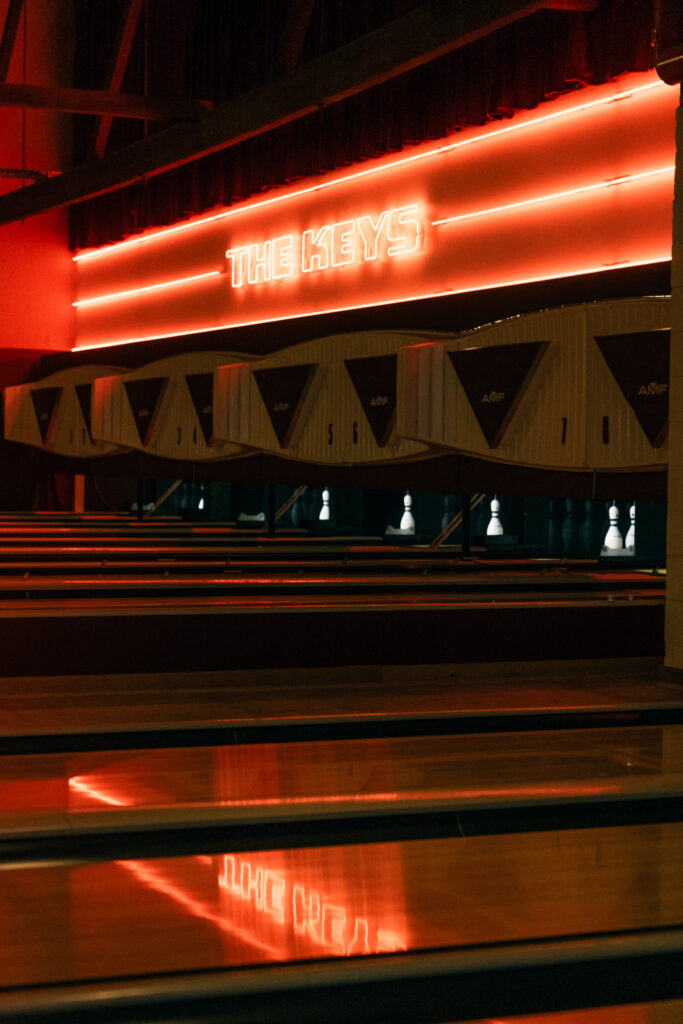 a red neon sign that says the keys and you can see bowling lanes and bowling pins