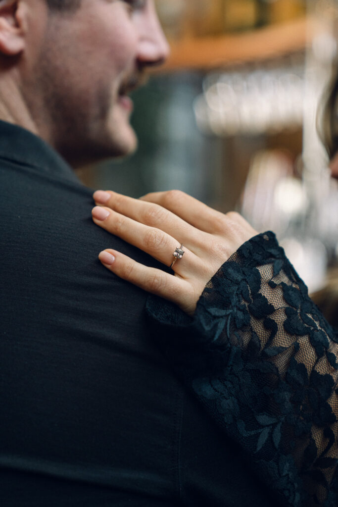 a couple sitting at a bar, her hand is on his shoulder and an engagement ring is visible