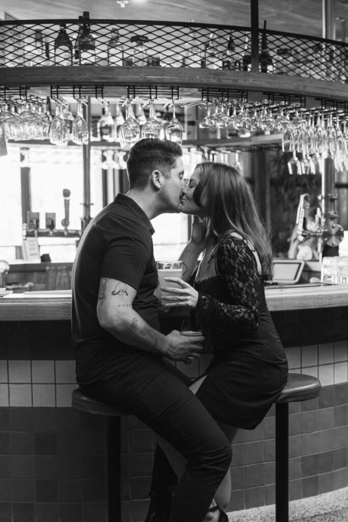 couple sharing a kiss at a bar while holding some beers