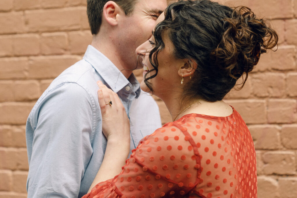 couple hugging in front of a colourful pink wall, an engagement ring is visible