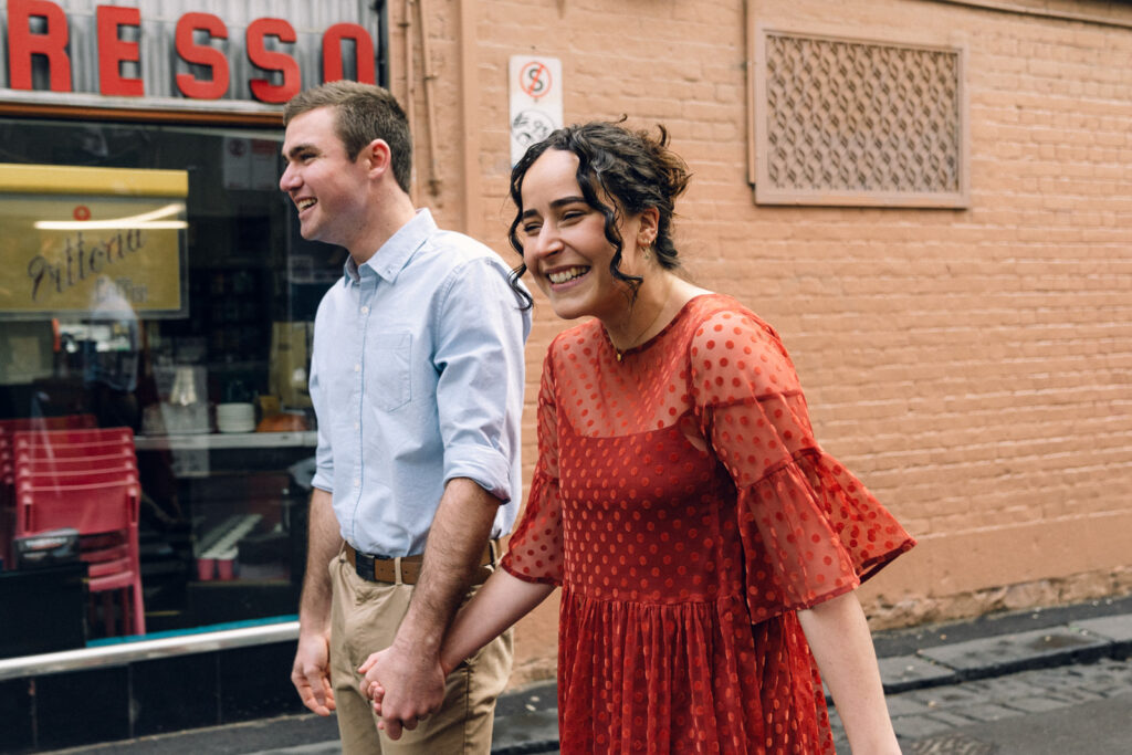 couple laughing and holding hands together in front of pellegrini's espresso bar