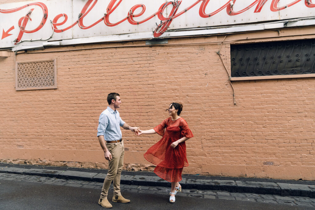 couple holding hands in front of a colourful pink wall for their engagement photos at Pellegrini's Espresso Bar