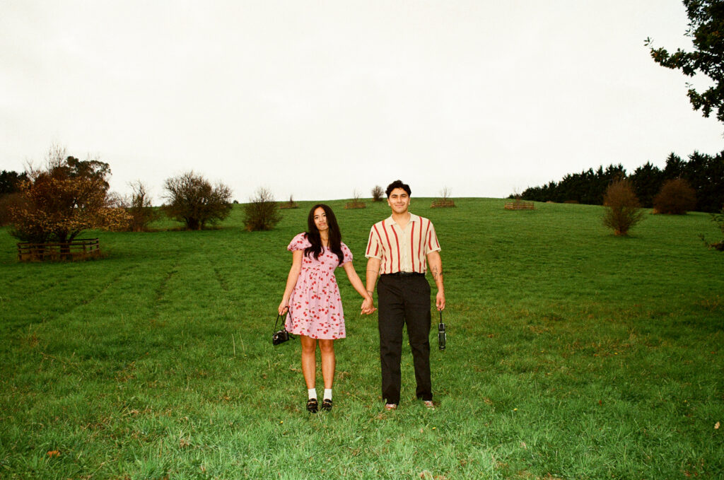 husband and wife holding hand in an open field while holding cameras