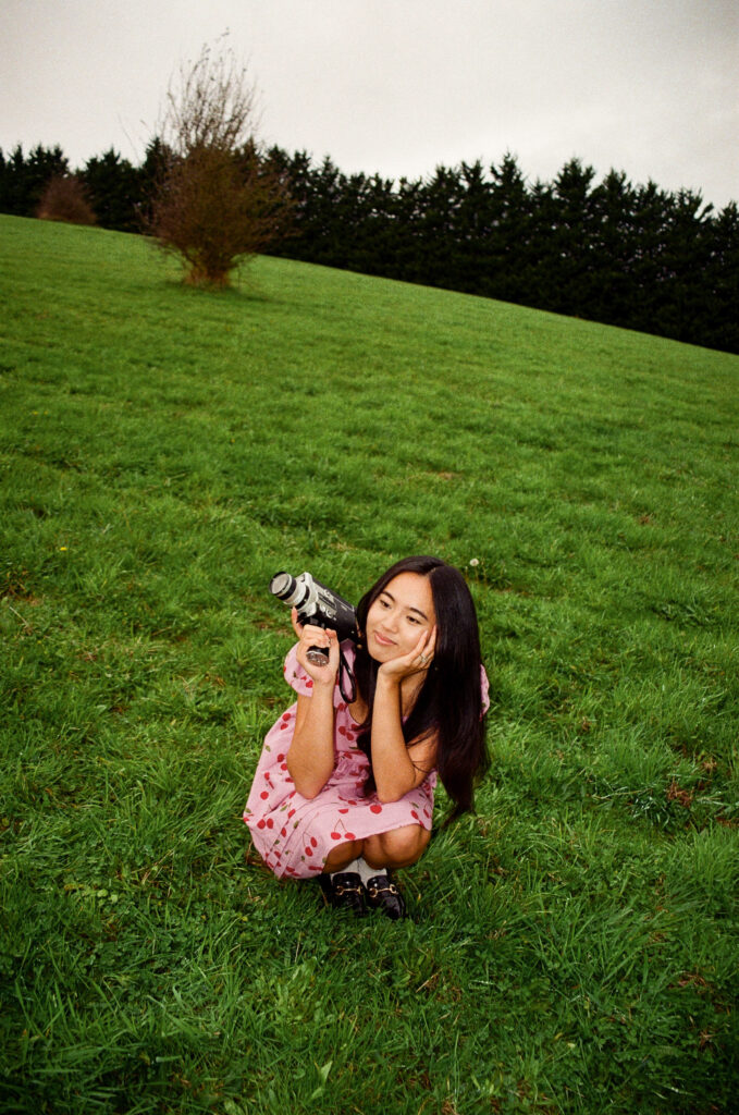 a woman holding a super 8 camera in the middle of an open field