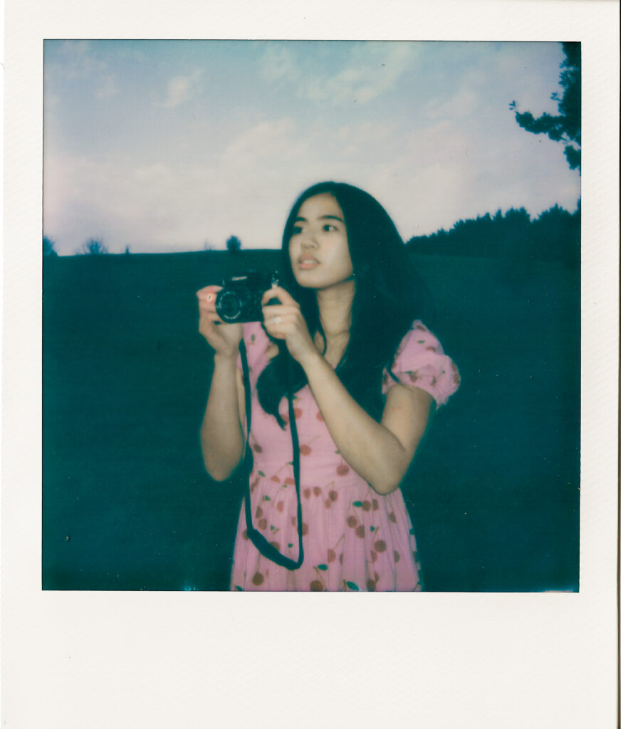 polaroid of a girl in a pink dress holding a film camera, 