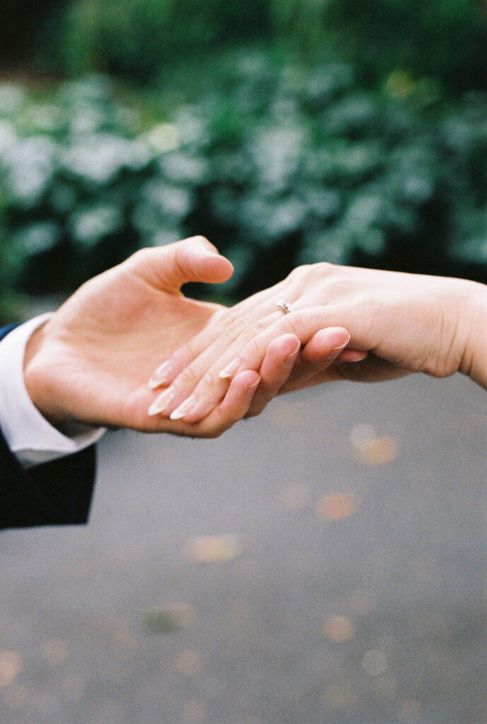 a close up film photo of a groom holding his bride's hand so you can see the wedding rings