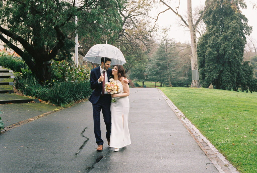 a couple walking and holding each other close under an umbrella during their elopement in melbourne