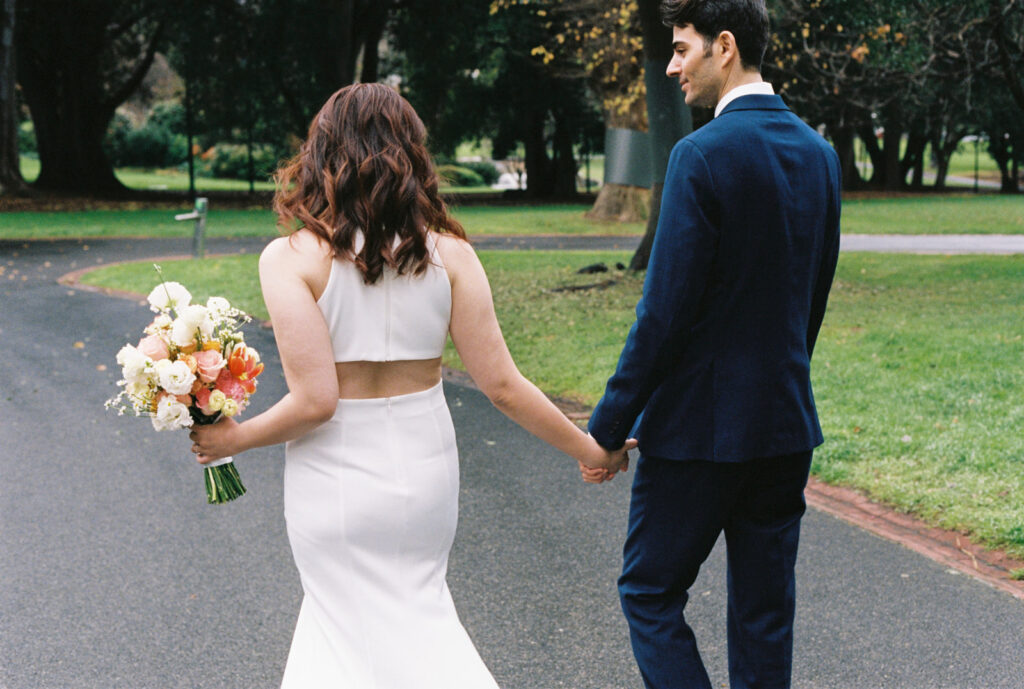 a couple holding hands on their wedding day in the treasury gardens