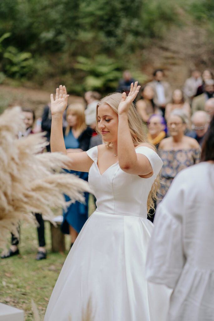 a bride lifting her hands in worship during her wedding ceremony, she is wearing a white silk ballgown style wedding dress