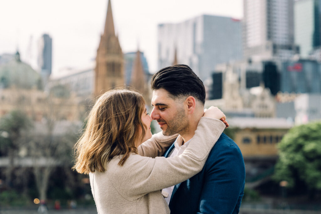 couple huggin and touchign their noses together, a blurry city scape is seen in the background