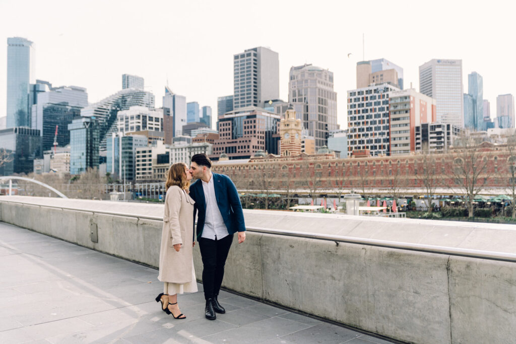 Couple kissing during their pre-wedding photography, southbank melbourne cityline is visible in the background