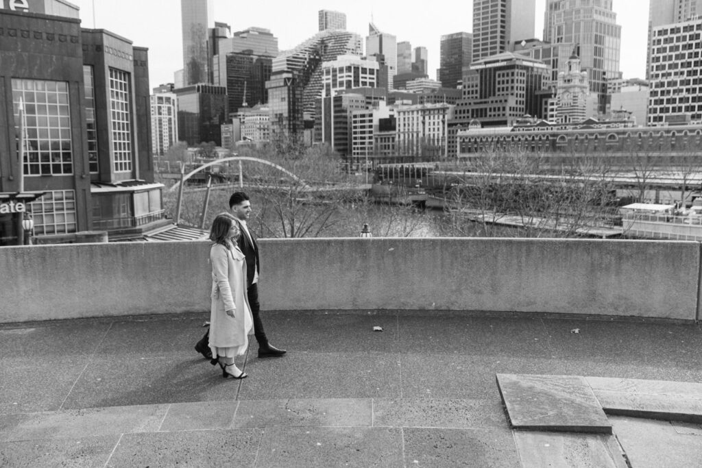 A black and white 35mm photo of a couple walking through melbourne city during their engagement photos