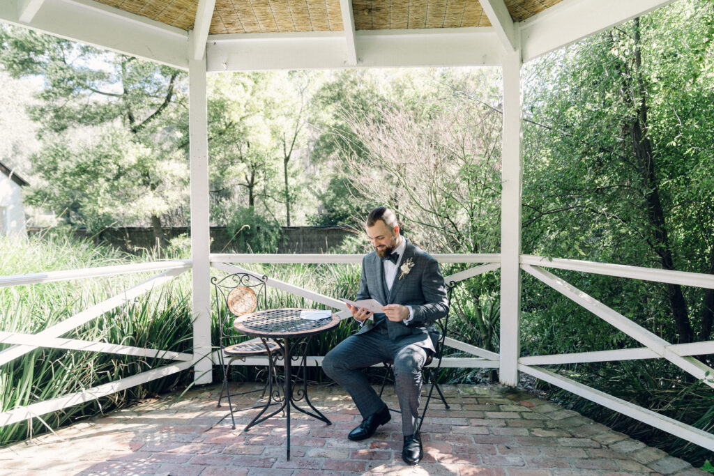 groom reading a letter from the bride in the potters receptions garden gazebo