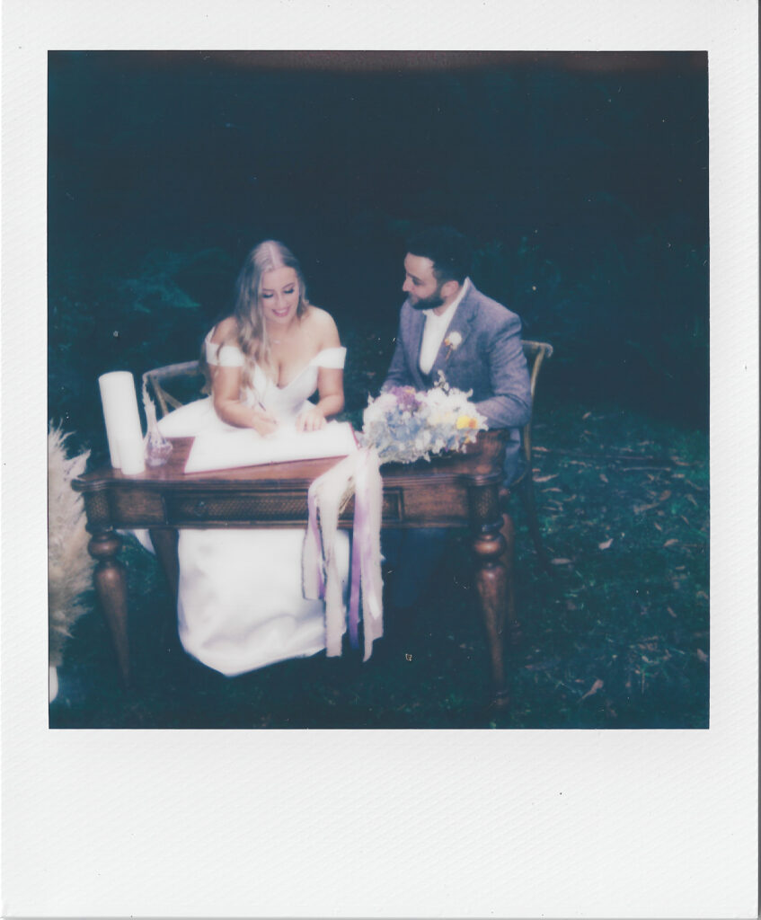 a polaroid of a couple signing their wedding certificate