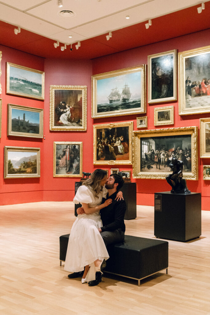 a couple sitting together in the middle of the red classic painting room at the national gallery of victoria