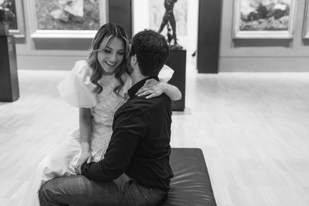 a black and white photo of a couple laughing together in the middle of an art gallery