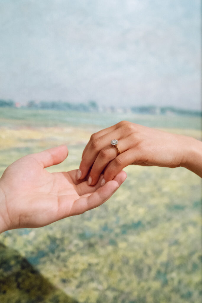 an up close photo of an engagement ring in front of a classic painting in the melbourne art gallery