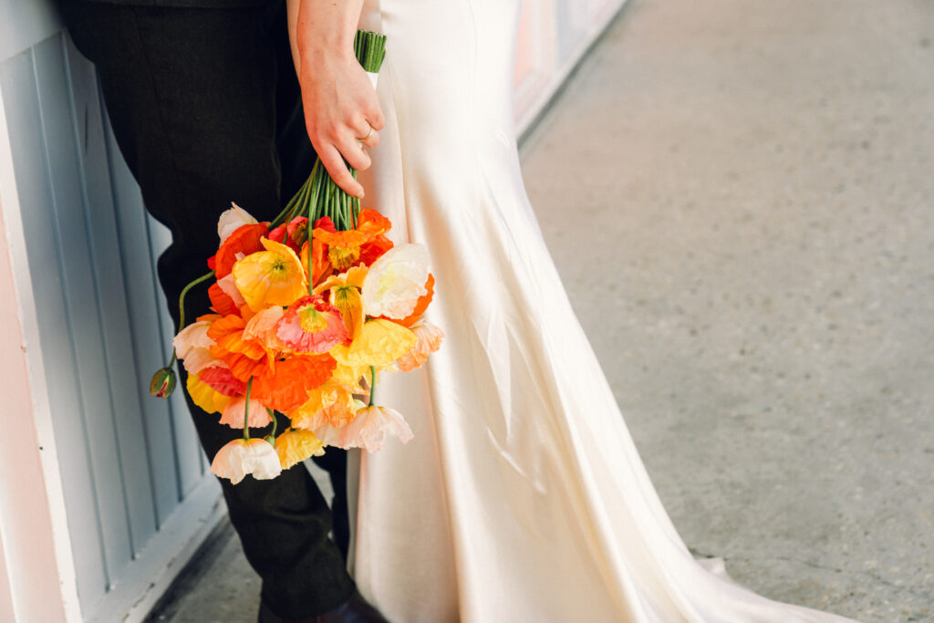 a closeup of the bouquet of orange poppies while the bride and groom cuddle