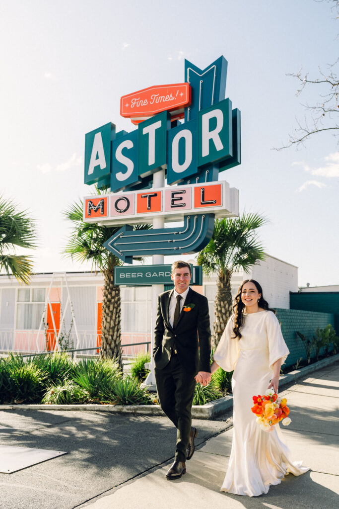 bride and groom walking hand in hand smiling in front of the astor motel sign