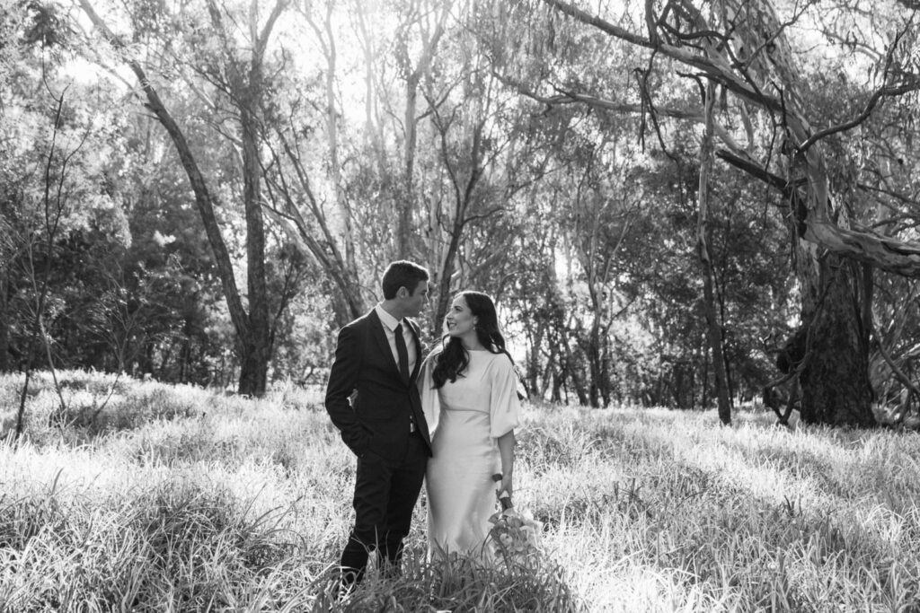 a black and white photo of a bride and groom standing in a forest near the murray river