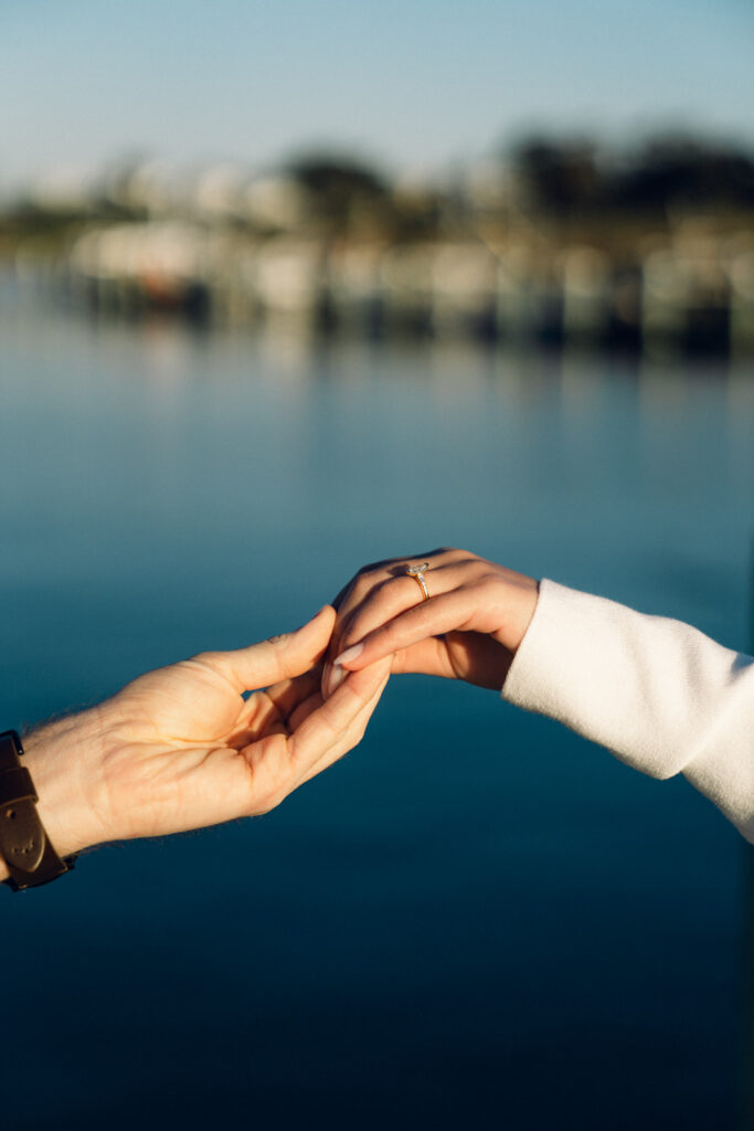 a closeup of an engagement ring with the beach in the background