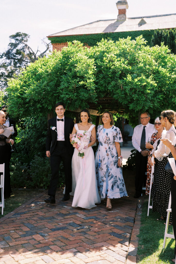 bride walking down the aisle with her brother and mum