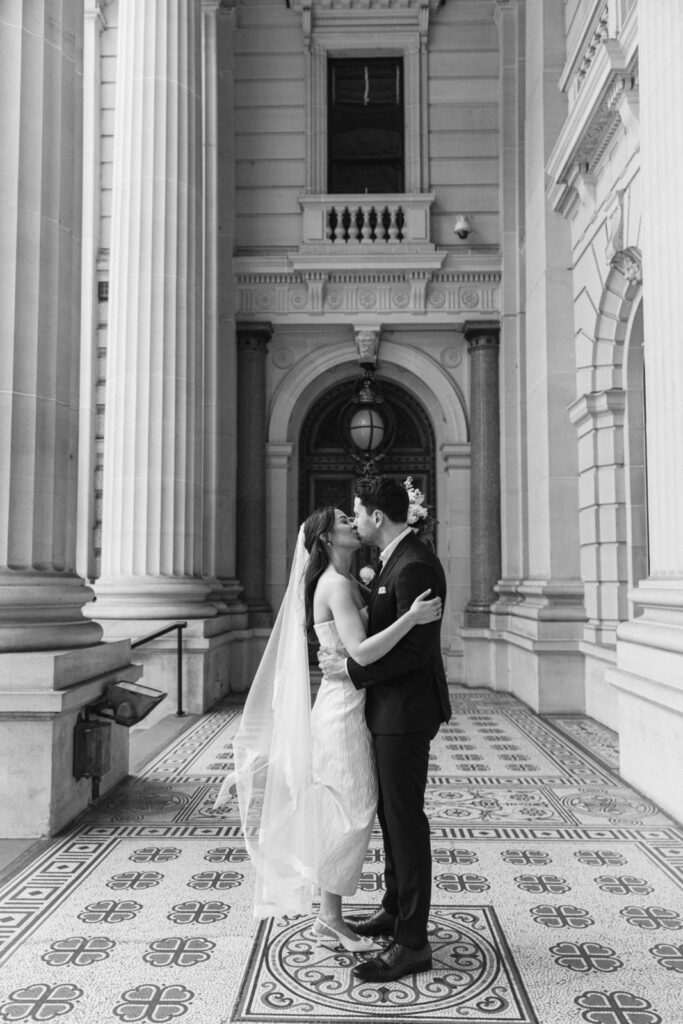 black and white photo of a bride and groom kissing at the parliament house in melbourne