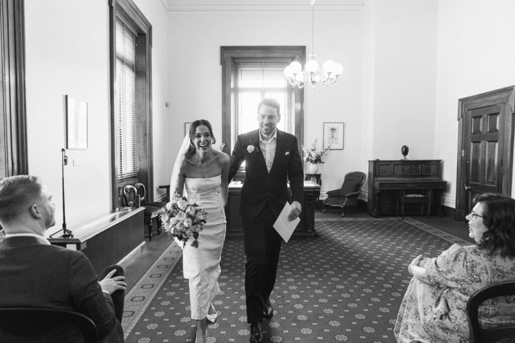 bride and groom smiling and walking down the aisle of the marriage registry building