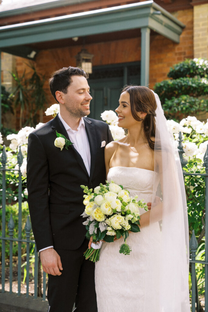 bride and groom smiling together in front of white roses