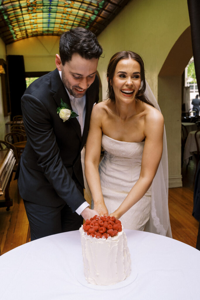 bride and groom laughing together and cutting their raspberry topped cake