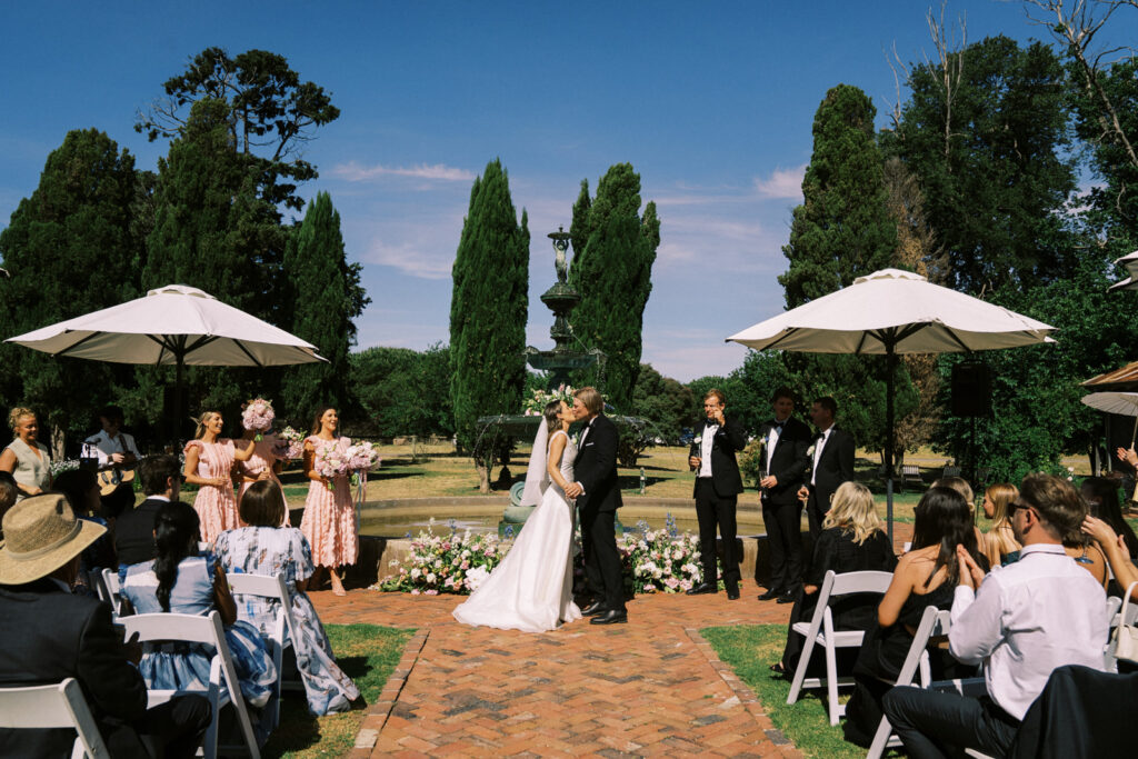 bride and groom kissing in front of the fountain of the main garden during their wedding ceremony