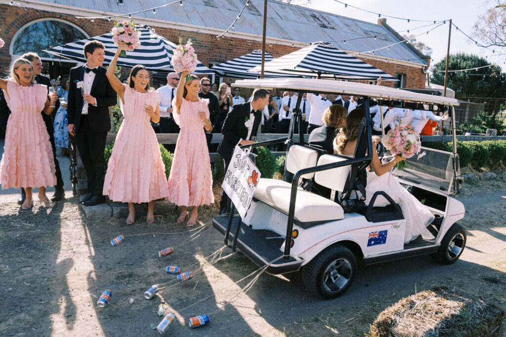 bride and groom driving past their guests on a "just married" golf cart