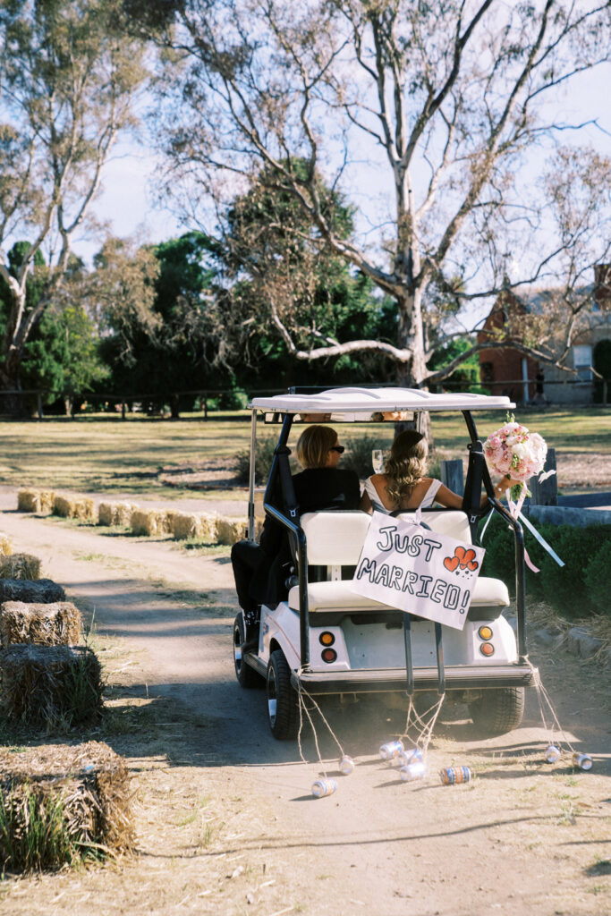 bride and groom driving away in a golf cart with the sign saying "just married" behind them