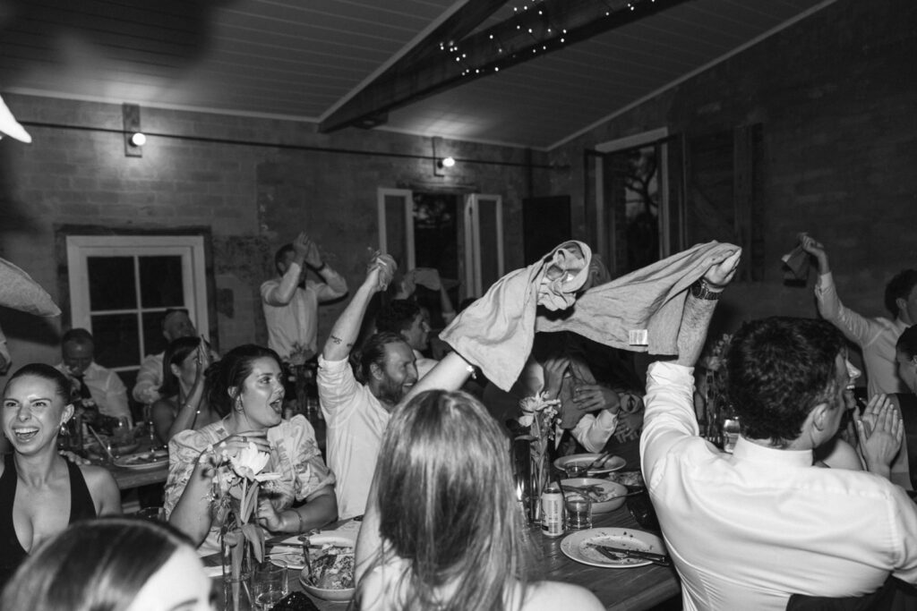 black and white photo of wedding guests throwing their napkins in the air and cheering