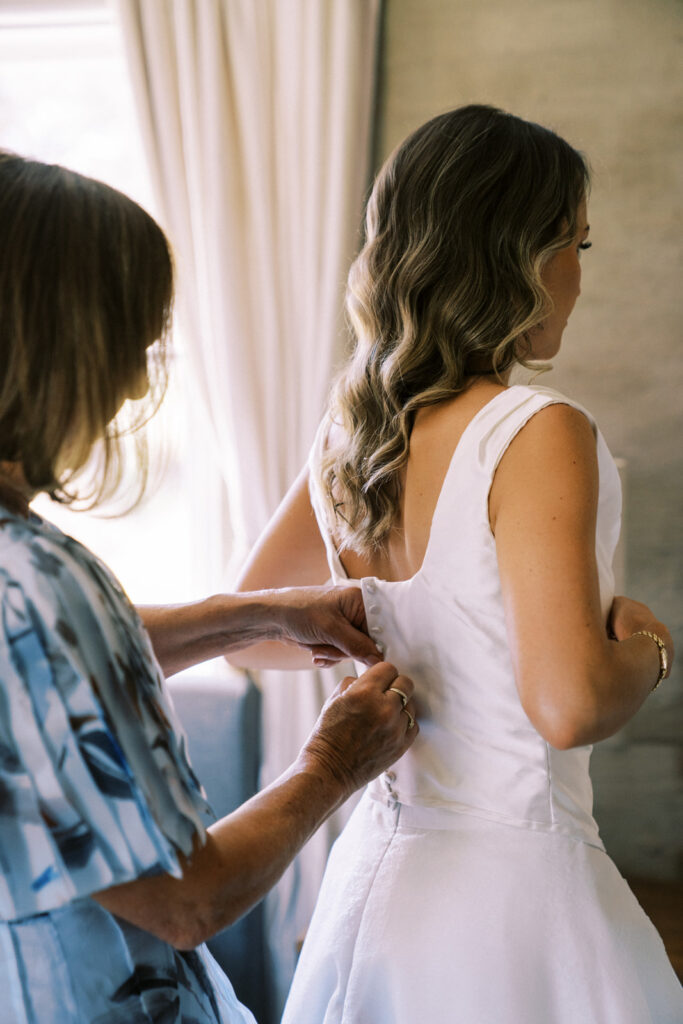 mother of the bride helping her fasten the buttons on her dress