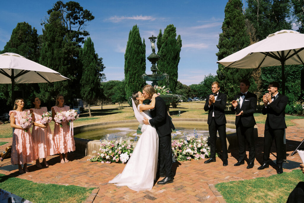 bride and grooms first kiss in front of the fountain in the main garden of Ravenswood Homestead